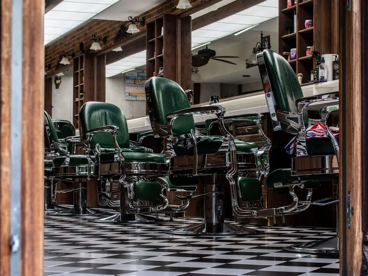 A row of empty green barber chairs in a barbershop.