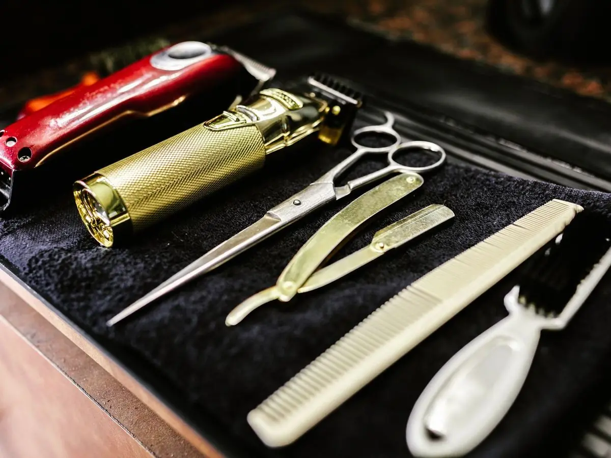 Barber clippers, scissors, a razor and a comb laid out on a towel.